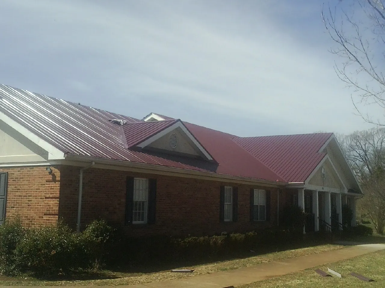 Red metal roof with gabled entries on a long brick building, from a Hail Damage Roof Repair job in Shade Gap