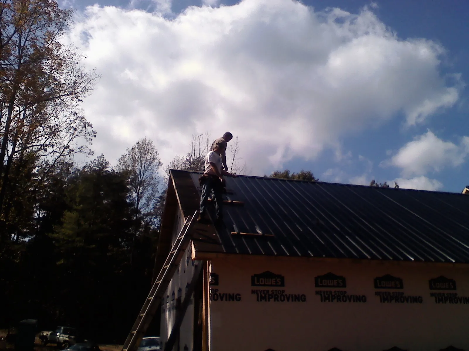 Roofer fastening dark metal panels high against a cloudy sky, from a Roof Inspection job in Shade Gap