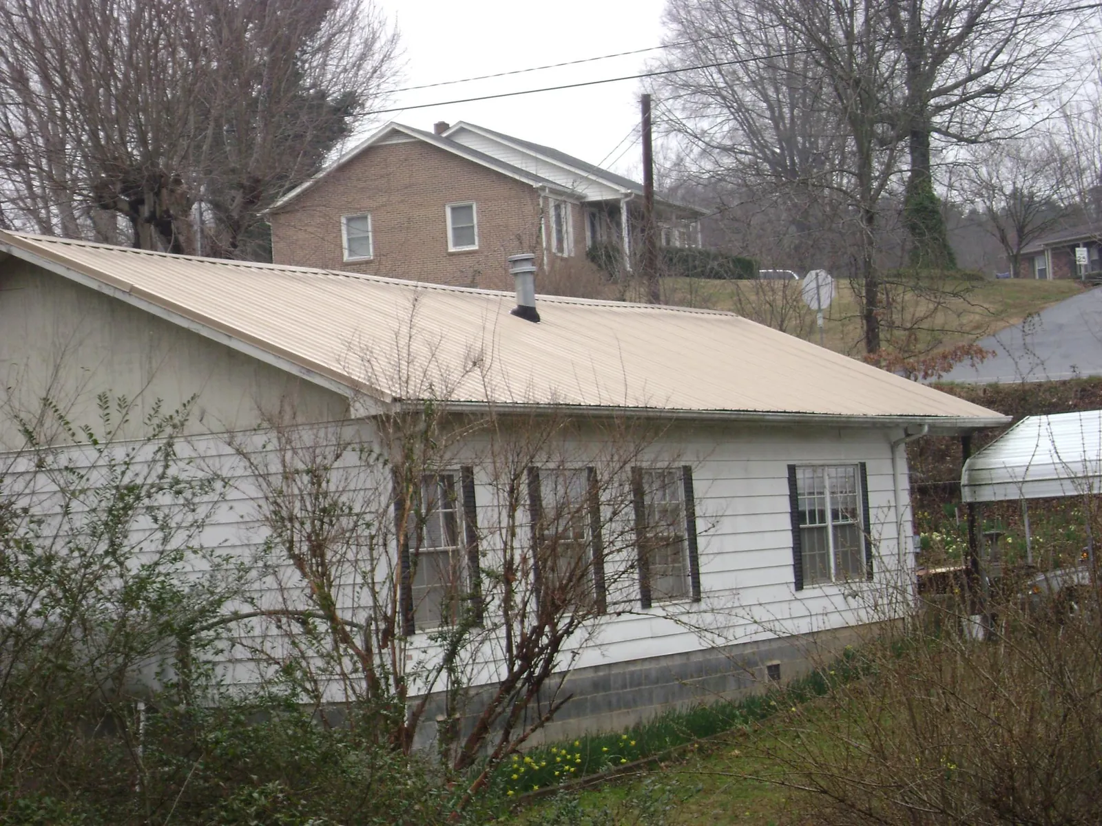 Tan metal roof on a white sided house set into a hillside — Commercial Roofing by Roofing Brothers in Shade Gap